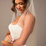 Woman wearing a white wedding dress with a veil against a neutral background