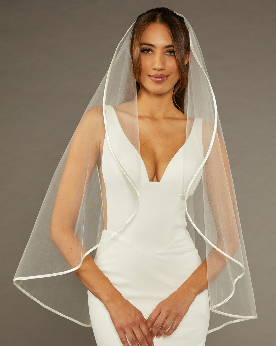 Simple Satin Trim Fingertip Bridal Veil Woman wearing a wedding dress with a veil against a brown background