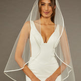 Simple Satin Trim Fingertip Bridal Veil Woman wearing a wedding dress with a veil against a brown background