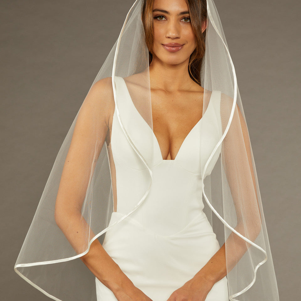 Simple Satin Trim Fingertip Bridal Veil Woman wearing a wedding dress with a veil against a brown background