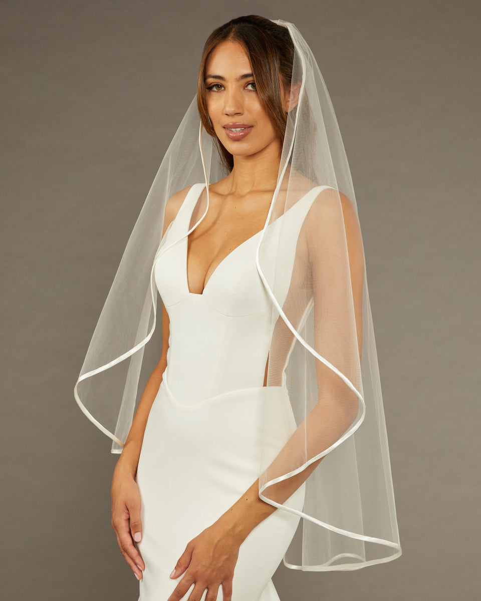 Simple Satin Trim Fingertip Bridal VeilWoman wearing a  wedding dress with a sheer veil against a brown background