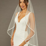 Simple Satin Trim Fingertip Bridal VeilWoman wearing a  wedding dress with a sheer veil against a brown background