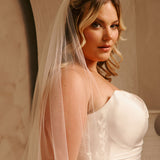Cathedral Bridal Veil with Lace Flowers and Sequins Cassandra Lynne A woman wearing a strapless wedding dress with delicate floral embroidery and a sheer white veil, posed against a warm beige background.