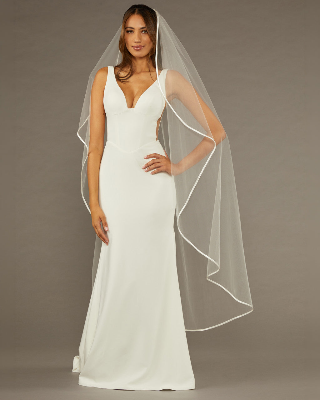 Waltz Waterfall Veil with Satin Ribbon Trim Woman wearing a wedding dress with a long veil against a brown background