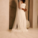 Bridal Veil with Double Crystal Trim A woman wearing a strapless ivory wedding gown with a long sheer veil, standing in a softly lit architectural setting with warm beige walls and arches.