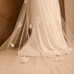 Bridal Veil with Painted Flowers and Pearls Cassandra Lynne - A close-up of a bridal veil with delicate ivory floral lace appliques, draped over a white wedding gown against a warm, neutral background.